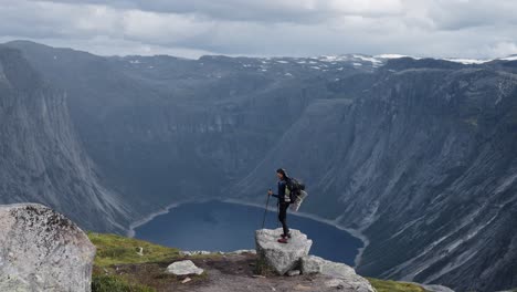 hiker on rocky peak overlooking deep blue fjord in norway, moody and majestic view