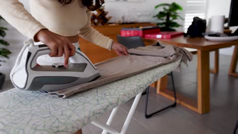a woman irons pants on a board in a bright, modern room with natural lighting and minimalistic decor