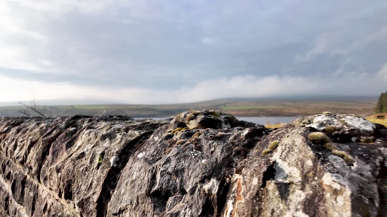 A weathered stone wall frames a quiet rural landscape under an overcast sky
