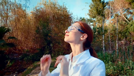 a young woman scientist at a creek, wearing a lab coat, smiles and puts on her lab glasses, then looks forward with a nod of confidence and satisfaction