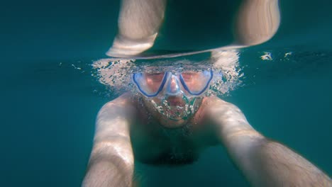 toma submarina de mano de un hombre que se filma a sí mismo mientras nada con una máscara de buceo