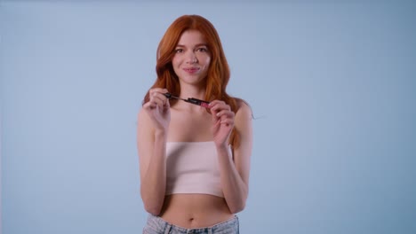 young redhead woman with fair skin applies mascara expressively and looks directly into the camera with confidence.