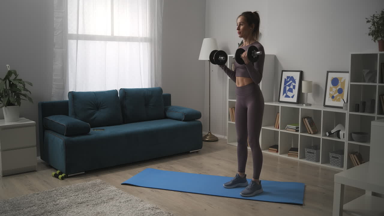 mujer delgada está levantando pesas en la sala de estar entrenamiento de bíceps en casa para una buena forma del cuerpo en el hogar entrenamiento diario en el apartamento fitness y bienestar estilo de vida saludable