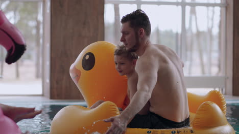 family is spending weekend in water park father and son are riding inflatable duck and splashing water