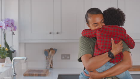 loving mother carrying and hugging son at home in family kitchen