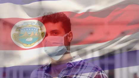 Animation-of-flag-of-costarica-waving-over-latin-man-wearing-face-mask-in-city-street