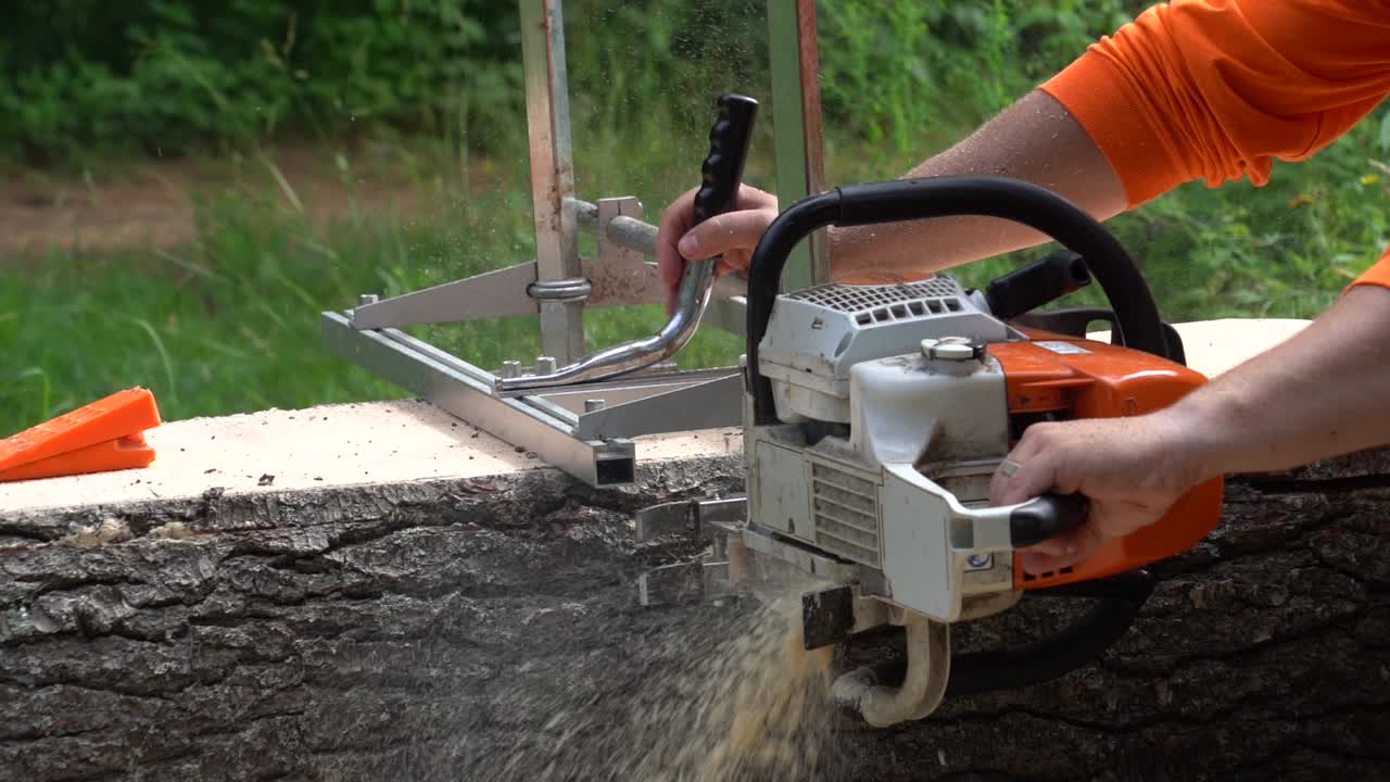 slow motion side shot of a logger wearing orange prepping a live-edge board from a pine log using an Alaskan chainsaw mill