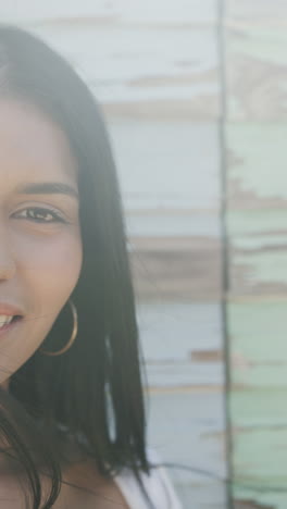 vertical video portrait of smiling biracial woman against weathered wood wall in sun, slow motion