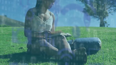 animation of technological icons over woman sitting on grass reading book in park