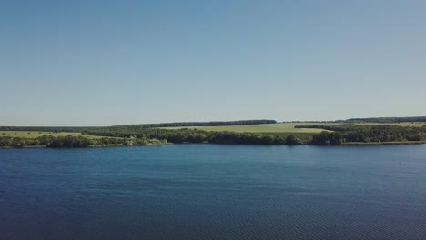 river with waves on the background of the shore with trees and a field on a summer day