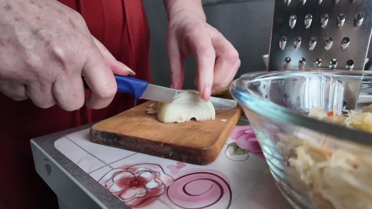 An elderly woman dices an onion for a healthy vegetable salad