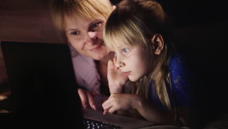 Junge-Mutter-Zusammen-Mit-Tochter-Spielen-Zusammen-Auf-Dem-Laptop-Neben-Dem-Bett-Liegend-Das-Licht-Von