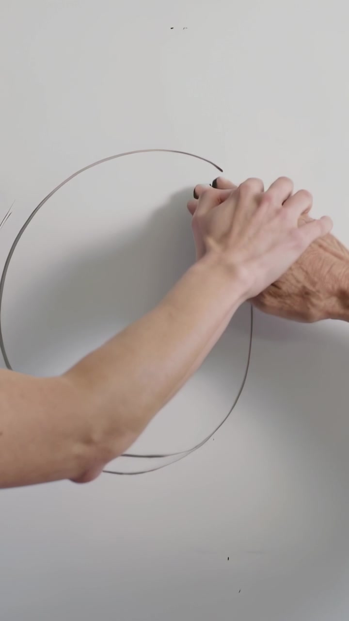 Video verticale: Due braccia che tracciano un arco con un pennarello su una lavagna bianca, completando un cerchio, con manica beige.