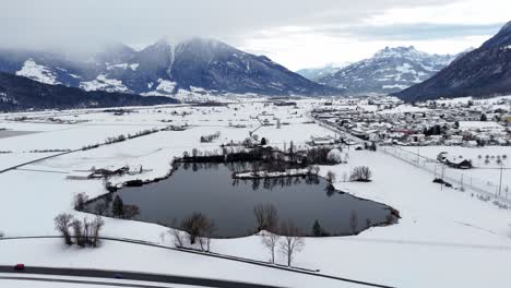 Toma-Aérea-De-Establecimiento-Del-Lago-Rodeado-De-Un-Paisaje-Nevado-De-Invierno-Y-Alpes-Suizos-En-El-Fondo