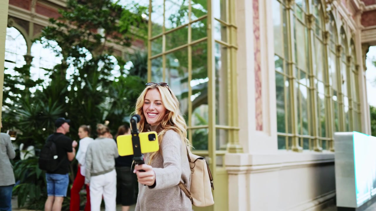 Donna sorridente che fa vlogging con smartphone mentre entra in serra