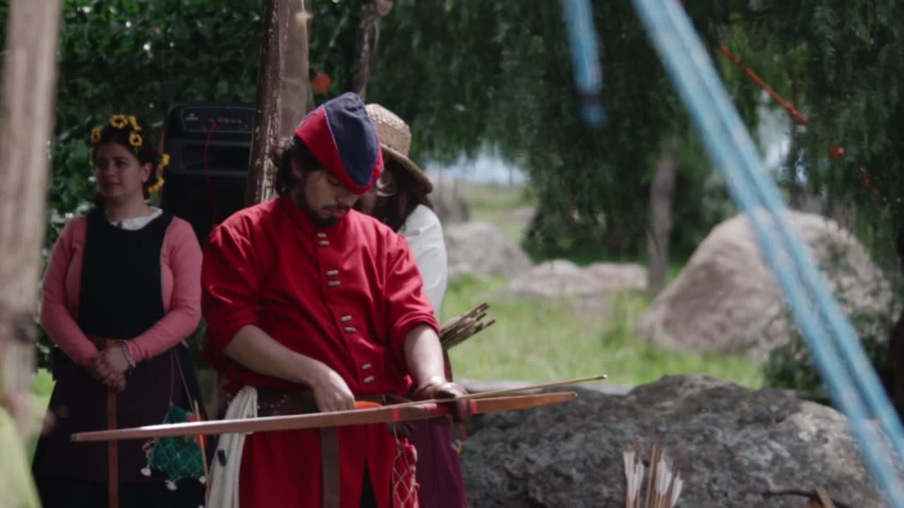 Medieval archer in red tunic shooting an arrow during a reenactment event, surrounded by onlookers