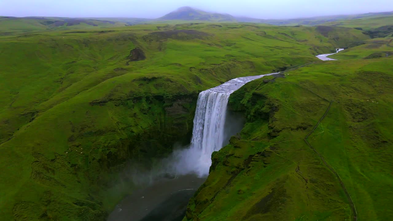 Discover the serene beauty of Skógafoss waterfall, as the drone flies over the cascading water and lush surroundings, inviting viewers into a world of Icelandic magic.