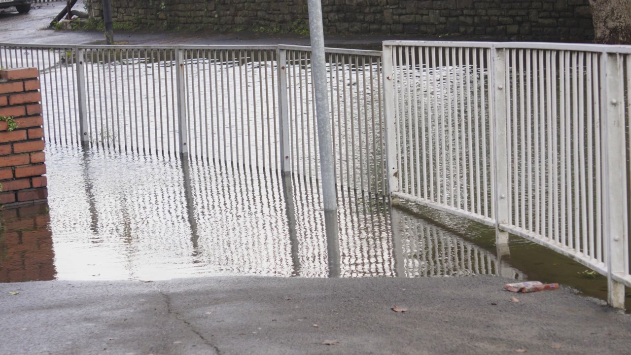 Flooded Pavement with Metal Rails Underwater with Road in Background Submerged After Excessive Rain Downpour. Flood in Swansea, UK.