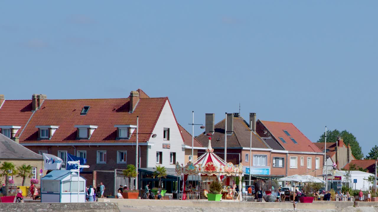 Daytime camera pan reveals carousel, beach, and townhouses under clear blue sky, steady movement