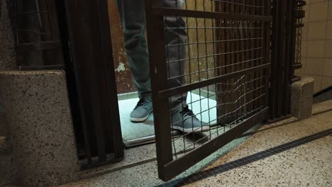 man in antique elevator descending and arriving at the floor of a building, getting out and shutting the wooden door and grid