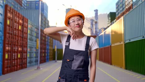 trabajadora asiática con gafas de protección y casco de seguridad limpiando el sudor y estando cansada mientras está de pie en el almacén del patio de contenedores