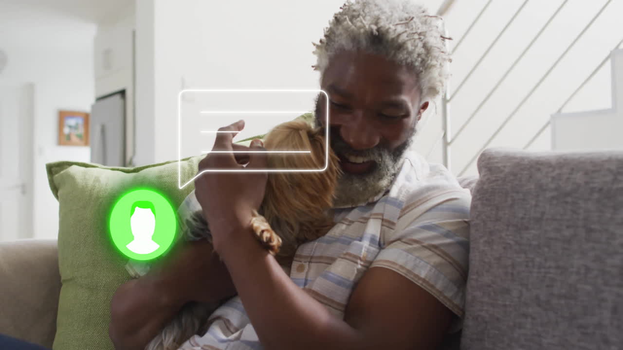 Man sitting hugging small dog on sofa in living room, displaying technology chat-bubble overlay