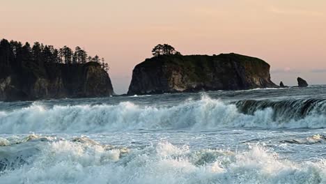 stunning slow motion shot of the beautiful ruby beach near forks, washington during golden hour with a small cliff island and large waves crashing into the shore