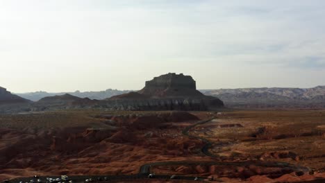 una escena del desierto de drones aéreos en ascenso con un camino estrecho y sinuoso rodeado de rocas rojas y arena con grandes formaciones rocosas de butte rojo y blanco en el fondo en el parque estatal goblin valley utah