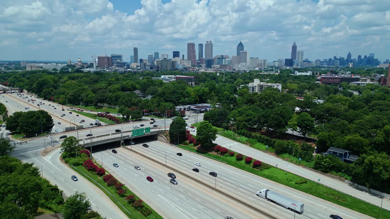 Busy traffic on interstate with green trees in suburbia of Atlanta, Georgia. Aerial panorama wide shot. Skyline with skyscrapers of metropolis in distance. Downtown in Atlanta city. Cloudy summer day