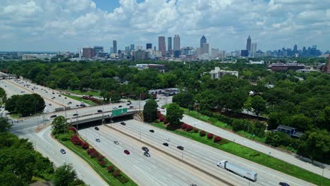 busy traffic on interstate with green trees in suburbia of atlanta, georgia. aerial panorama wide shot. skyline with skyscrapers of metropolis in distance. downtown in atlanta city. cloudy summer day