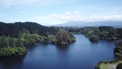 Drone-shot,-flying-over-lake-towards-forest-with-Mount-Taranaki-at-the-back,-in-New-Plymouth,-New-Zealand