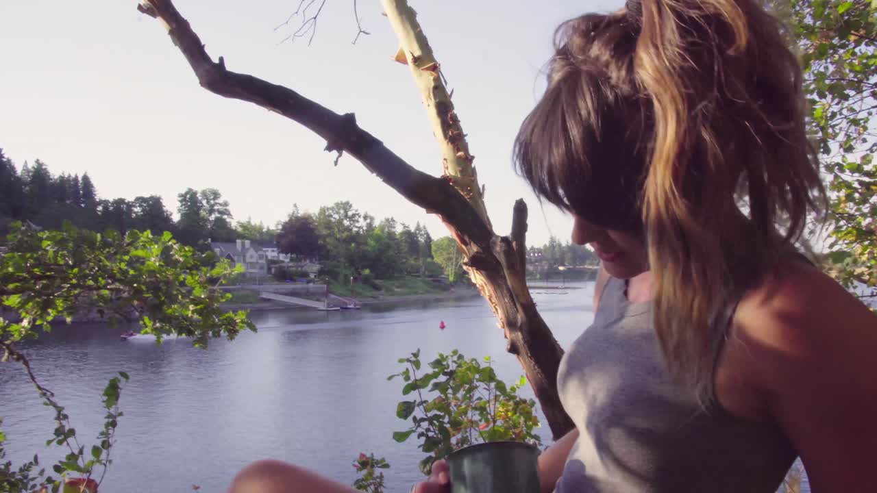 귀여운 힙스터 소녀가 머그컵에서 술을 마시고 지역 공원에서 물가에서 휴식을 취합니다.