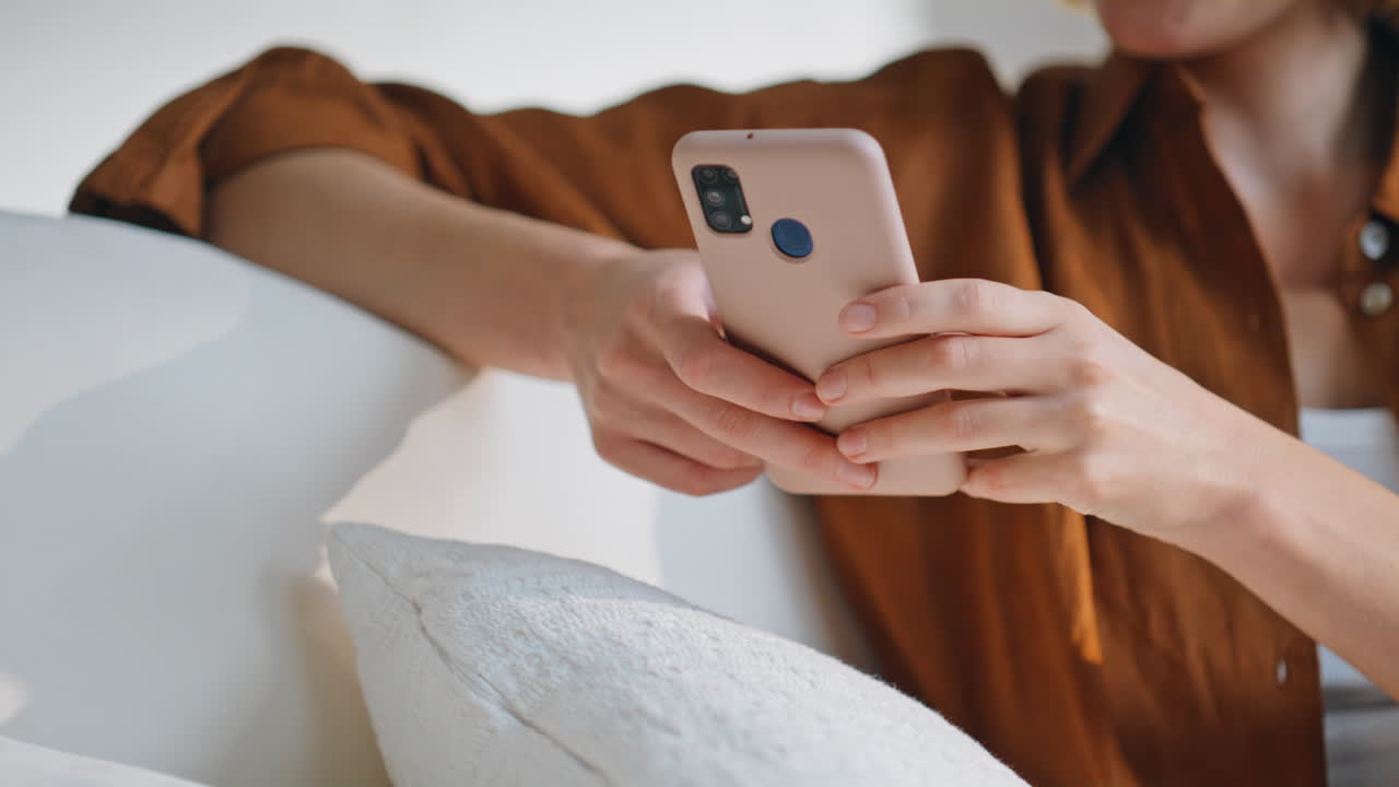 Woman hands typing smartphone in living room sofa closeup. Happy lady messaging