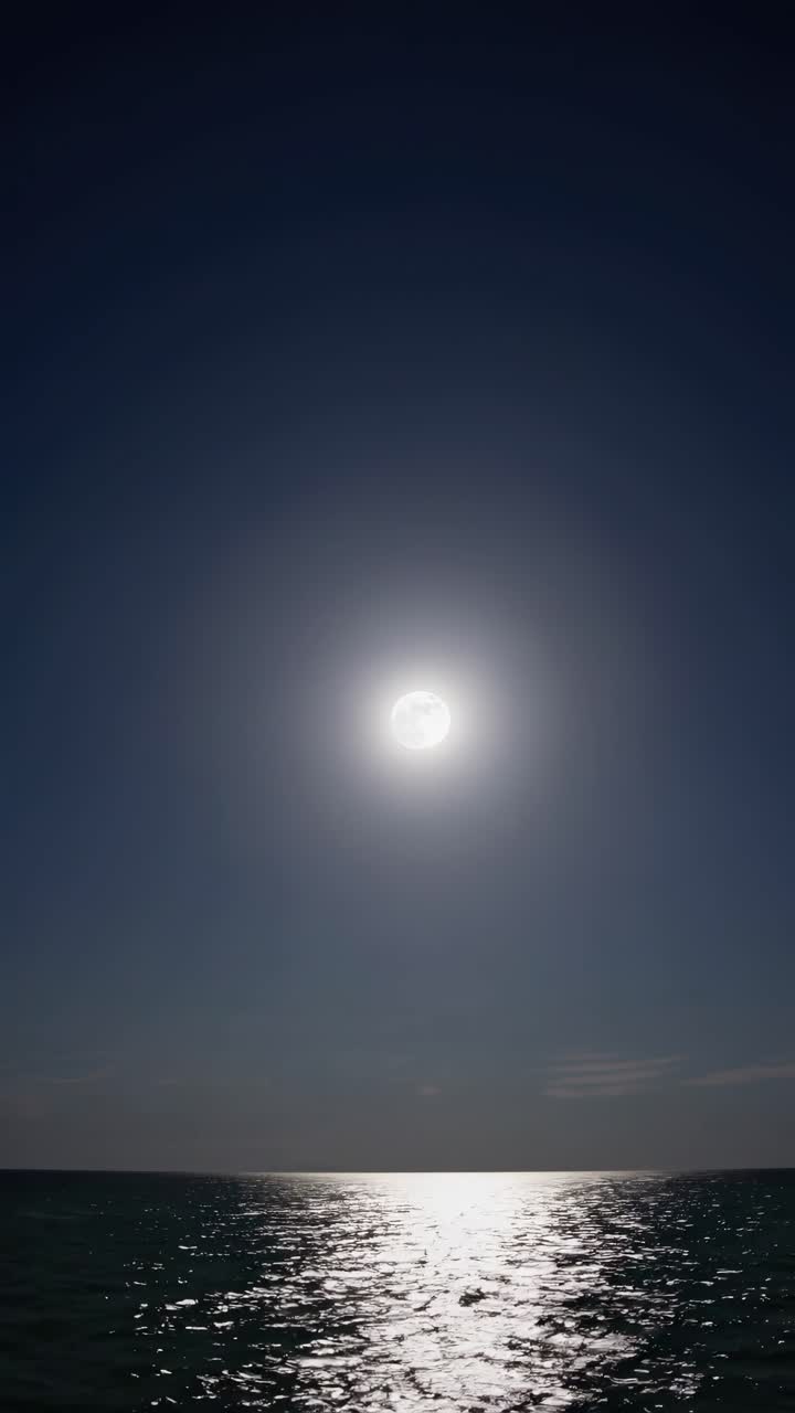 A serene video of a full moon reflecting on the ocean, captured from a low angle