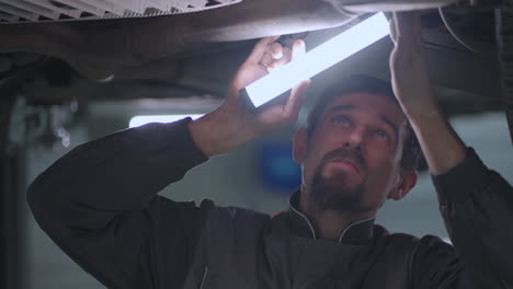 retrato del mecánico inspeccionando el coche desde abajo levantado en el ascensor e inspeccionando la parte inferior