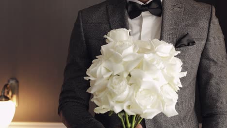 groom in a suit holding a bouquet of white roses