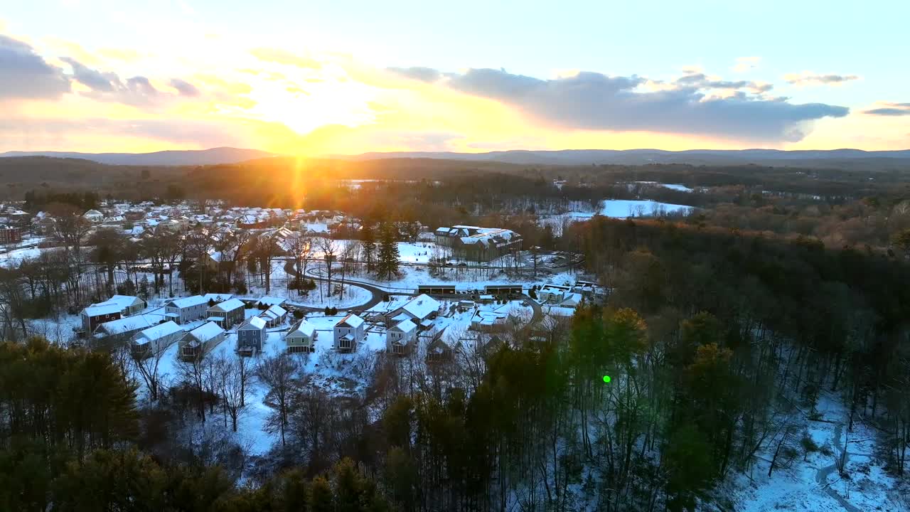 American suburb district with snowy houses and homes during golden sunset. Northampton Town, Massachusetts between leafless trees in Winter season. Aerial Wide shot.