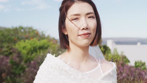 행복 한 아시아 신부 의 비디오 초상화 는 야외 결혼식 에서 카메라 에 미소 짓는 꽃줄 을 들고 있다