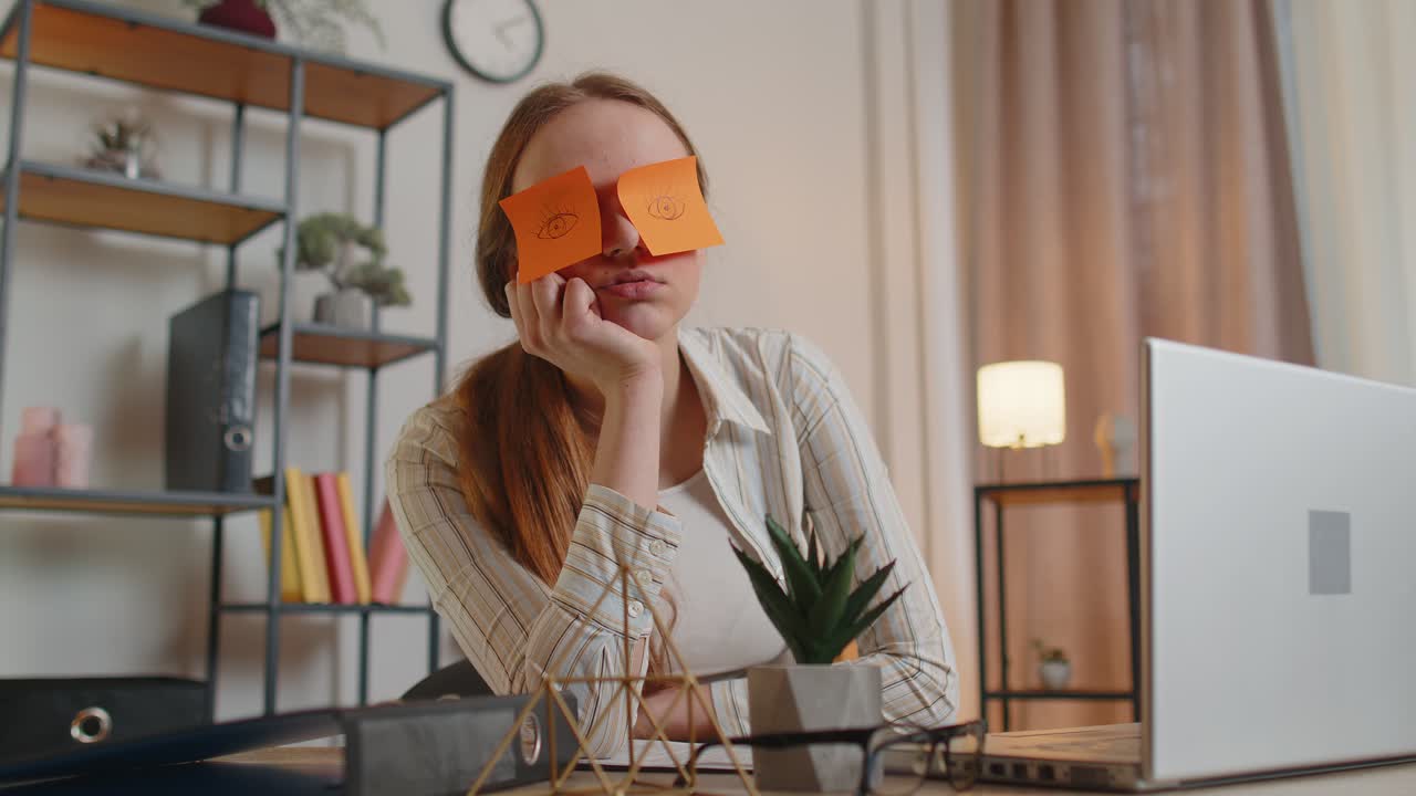 Tired woman teacher using laptop computer with funny stickers on eyes sleeps at workplace napping