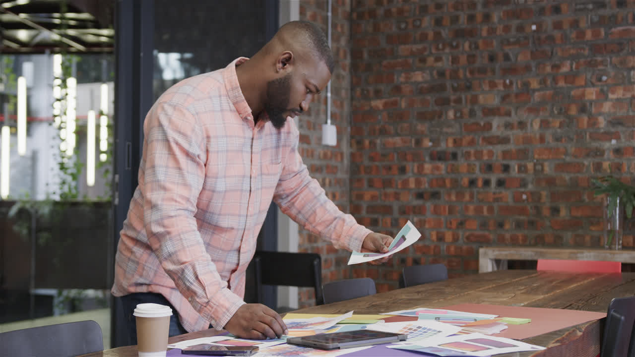African american male creative looking at designs in office, slow motion