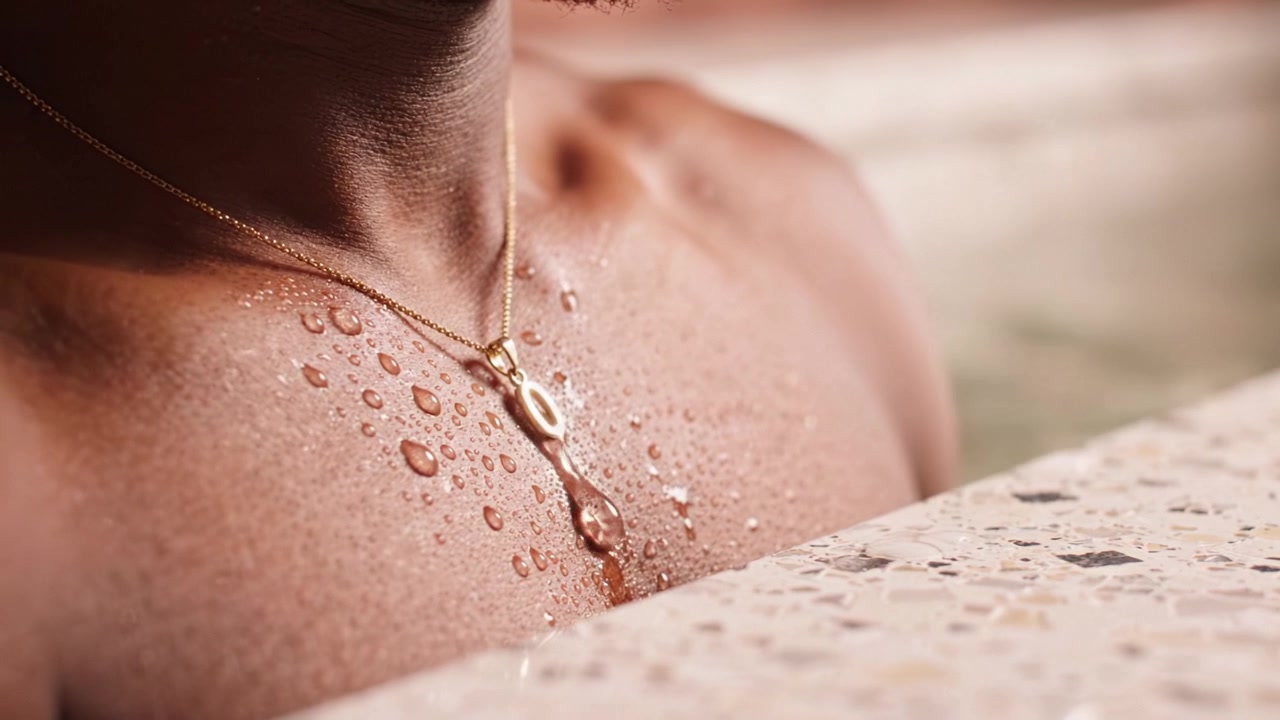 Primo piano di un petto lucido con gocce d'acqua e una collana scintillante in un ambiente rilassante, che cattura l'essenza della calma e della serenità.