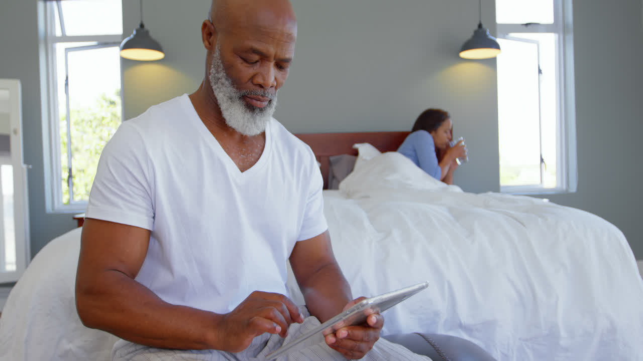 Front view of mature Caucasian man using digital tablet in bedroom at a comfortable home 4k