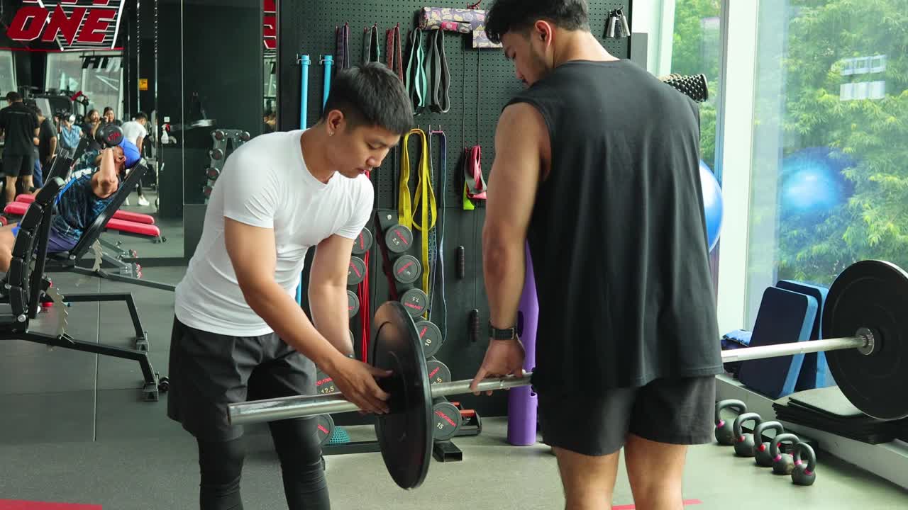 Personal trainer guides man setting up barbell for deadlifts in modern gym with daylight