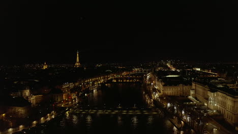 Forwards-fly-above-Seine-river.-Aerial-footage-of-traffic-and-illuminated-buildings-on-riverbanks.-Cone-from-spotlight-on-top-of-Eiffel-Tower-in-distance.-Paris,-France