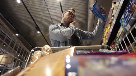 At-the-Supermarket:-Busy-man-in-glasses-with-shopping-cart-uses-smartphone---talking.-Looks-at-dairy-products-and-walks-through