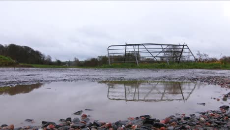 Raindrops-hit-a-puddle-in-front-of-a-gate-in-the-countryside