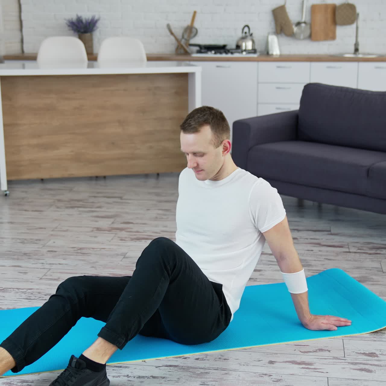 Man relaxes on a mat indoors. Young man sitting on a mat after hard workout at home. Fitness during quarantine