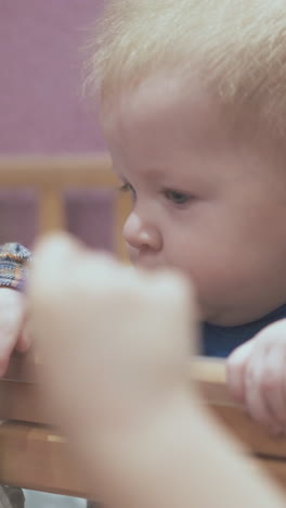 active little baby leans on wooden cot edge playing with blonde elder sister in light room closeup