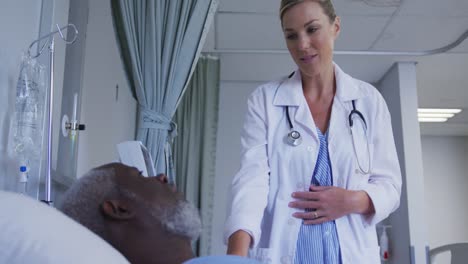 kaukasische ärztin spricht mit einem afroamerikanischen älteren männlichen patienten, der im krankenhaus im bett liegt