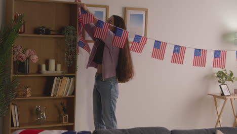 mujer en casa colgando estrellas americanas y rayas bandera bunting para la fiesta celebrando el 4 de julio día de la independencia 1